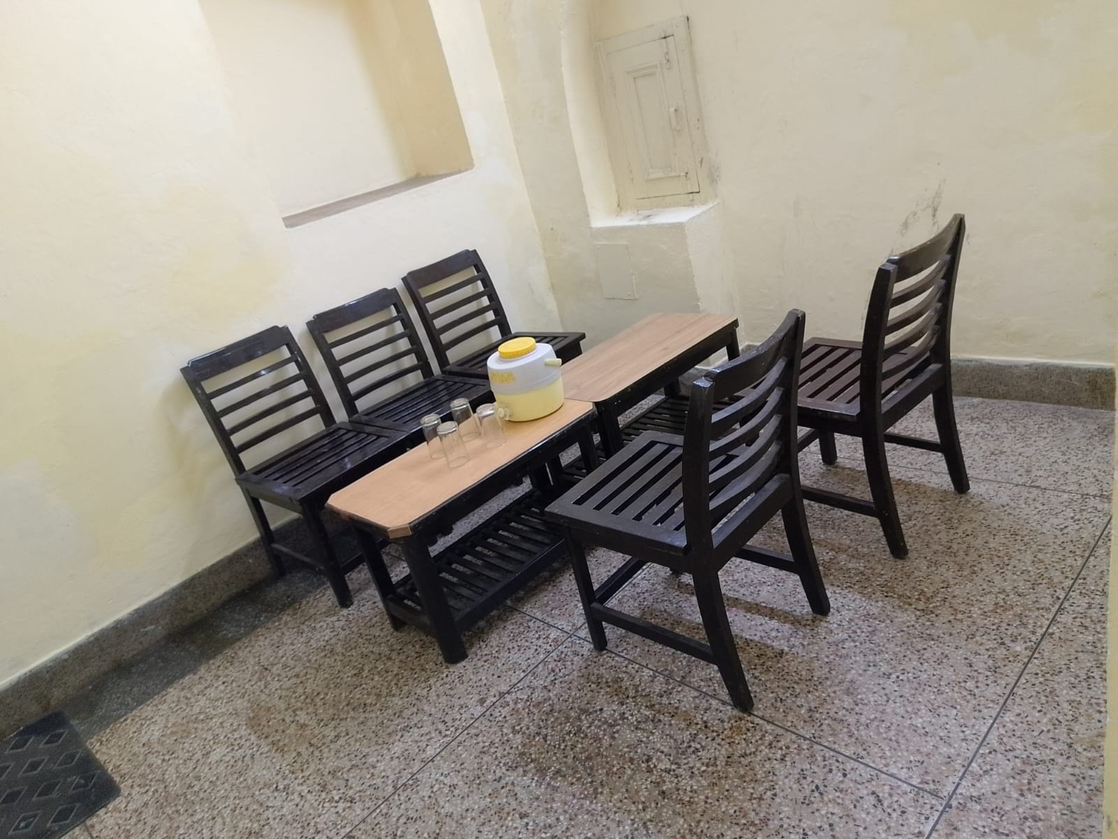 Un comedor con mesa y sillas de madera, un recipiente amarillo y un ventanal pequeño.