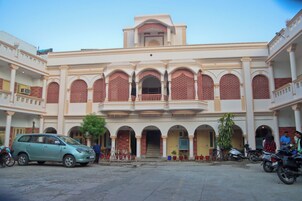 A building with multiple arches and a balcony, surrounded by parked vehicles and potted plants.