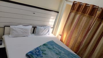 Een hotelkamer met een bed, witte kussens, een blauwe bloemenprint plaid en een gordijn.