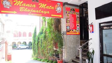 The entrance to Mansa Mata Bhujanalaya AC Restaurant with a staircase leading up to the entrance, a fire extinguisher mounted on the wall, and a menu board displaying various dishes.