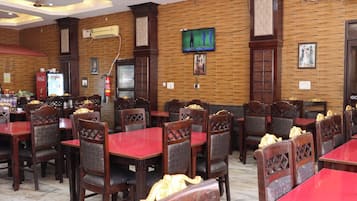 Un restaurante con paneles de madera, varias mesas y sillas, una pantalla de televisión y un extintor.