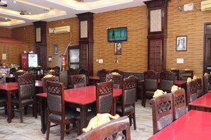 Un restaurante con paneles de madera, varias mesas y sillas, una pantalla de televisión y un extintor.