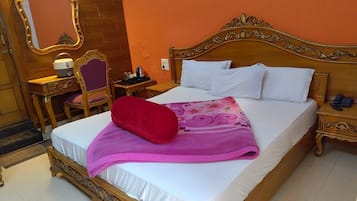 A hotel room with a large bed, a wooden nightstand, a desk with a chair, a mirror, and a red pillow.