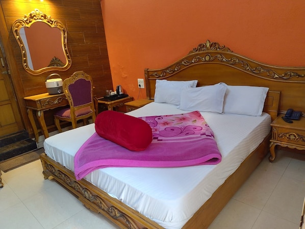 A hotel room with a large bed, a wooden nightstand, a desk with a chair, a mirror, and a red pillow.