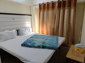 Une chambre d’hôtel avec un lit, une table de chevet dotée d’un distributeur d’eau et un rideau.