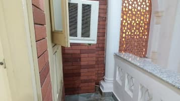 A narrow outdoor corridor with a brick wall, a white door, a window with blinds, and a white balustrade.