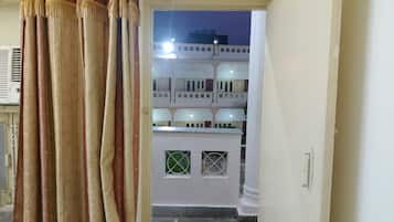 A doorway leading to a courtyard with a white building, a white door with a handle, and a window with a grid pattern.