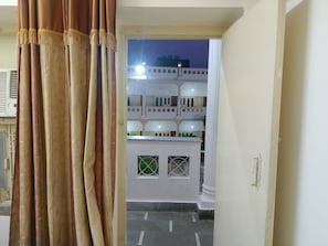 A doorway leading to a courtyard with a white building, a white door with a handle, and a window with a grid pattern.