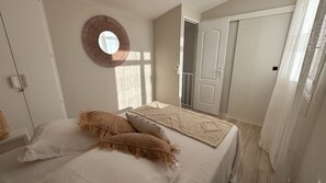 A bedroom with a bed, pillows, a wall-mounted mirror, and a wardrobe. - A LUMERIA Maison paisible 2 chambres avec clim et piscine partagée à Porticcio (Grosseto-Prugna)