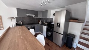 A modern kitchen with grey cabinets, stainless steel appliances, and a wooden dining table. - A LUMERIA Maison paisible 2 chambres avec clim et piscine partagée à Porticcio (Grosseto-Prugna)
