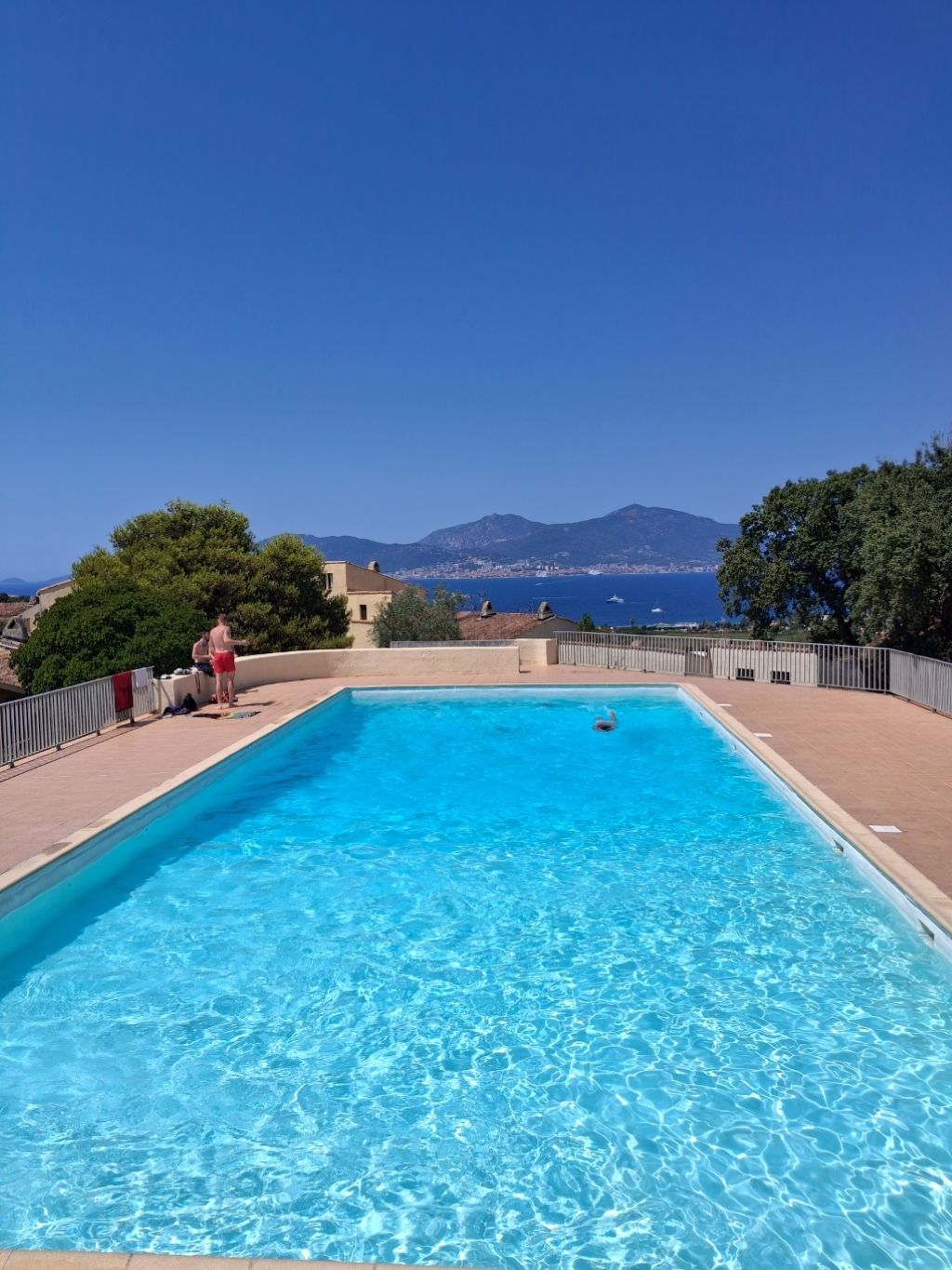 A rectangular swimming pool with clear blue water, surrounded by a tiled deck.