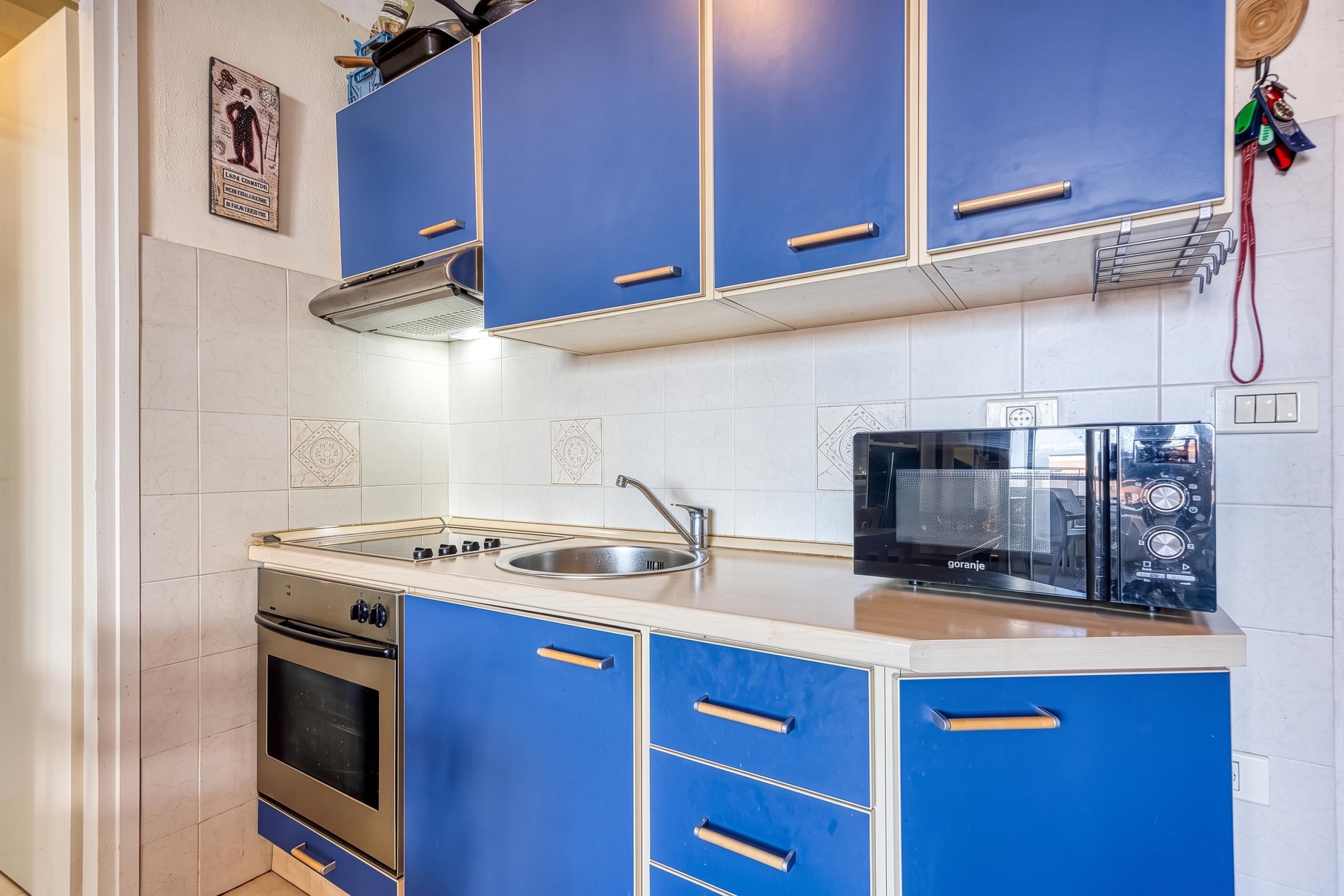 Una cocina con gabinetes azules, estufa, horno, pileta y microondas negro.
