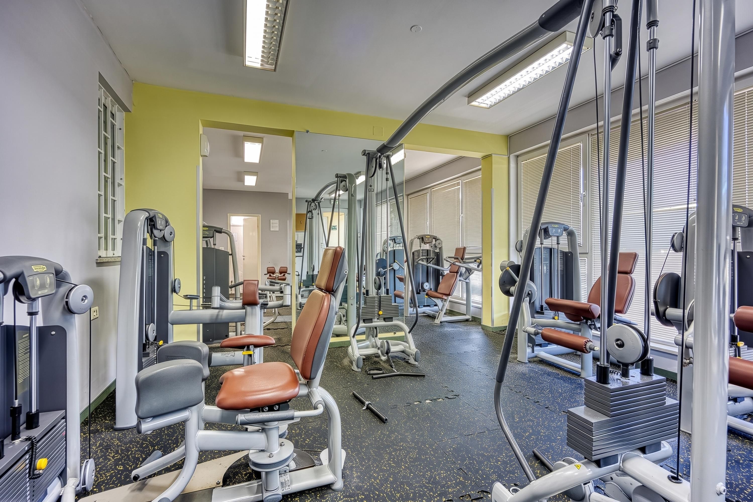 Une salle de sport équipée de divers appareils d’exercice, de miroirs et d’un mur jaune.