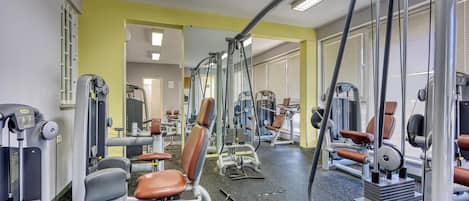 A gym with various exercise machines, mirrors, and a yellow wall.