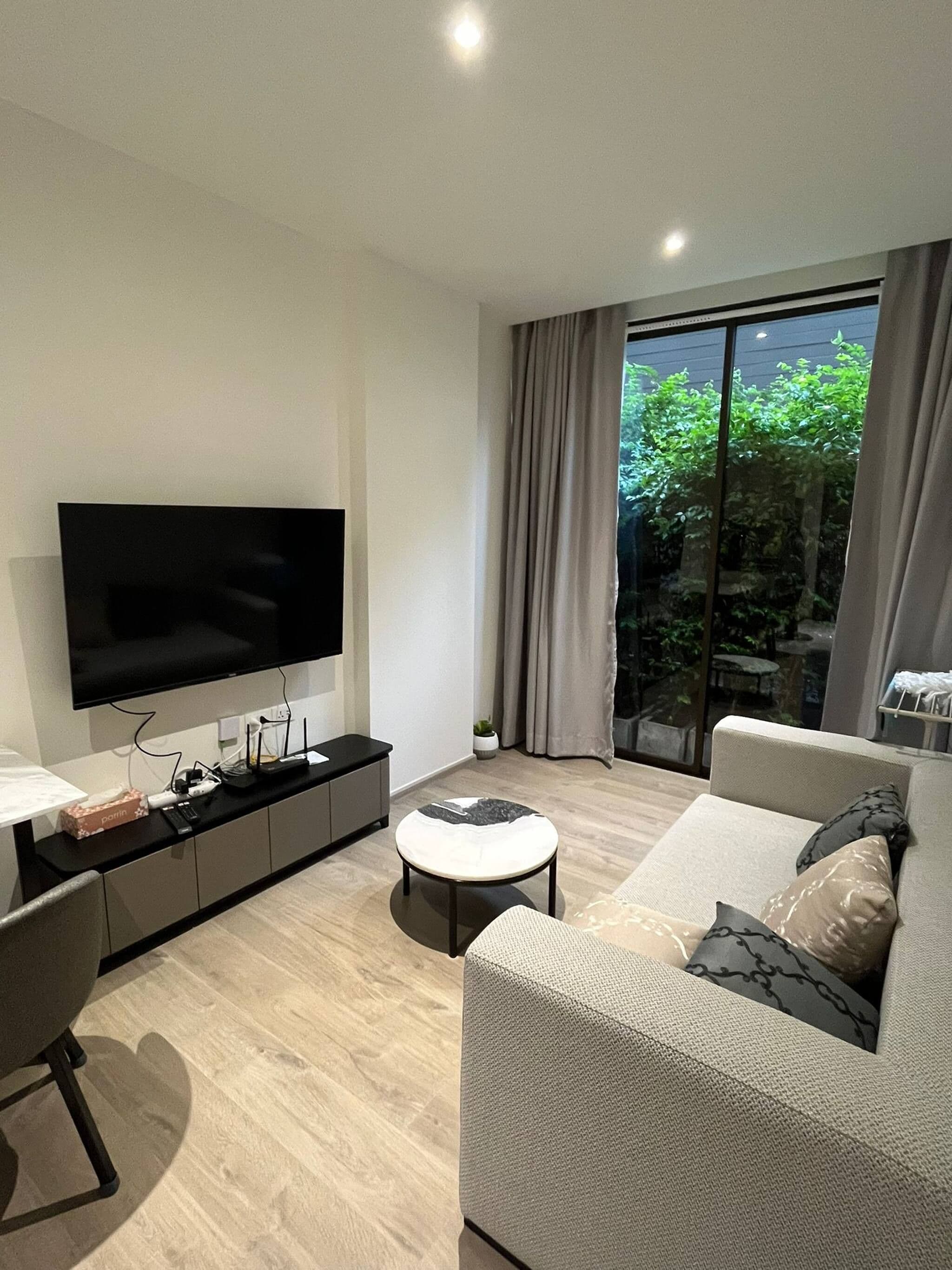 A modern living room with a flat-screen TV, a sofa, a coffee table, and a window with curtains.