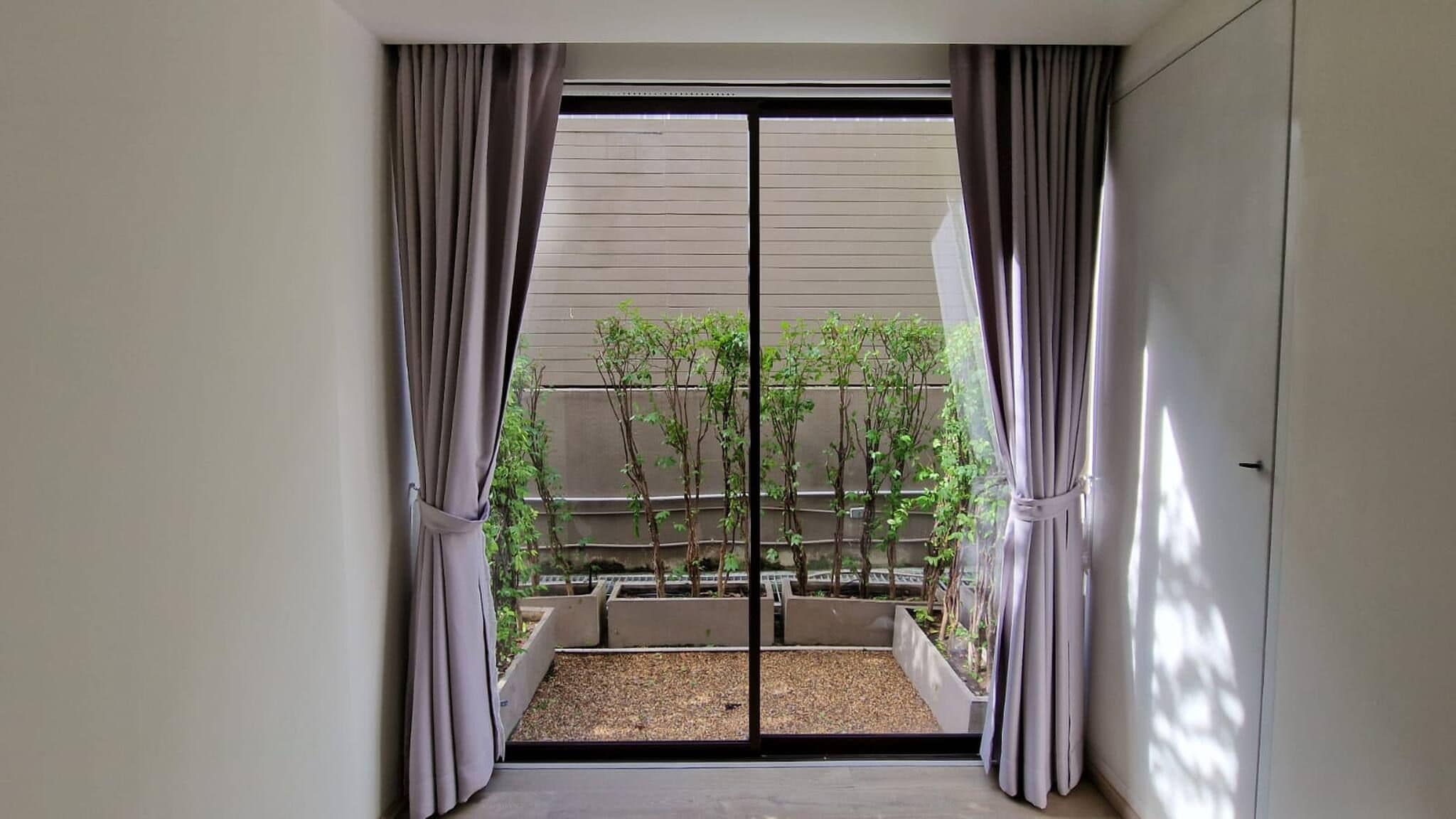 Vista a través de un ventanal corredizo a un balcón con plantas y zona de grava.