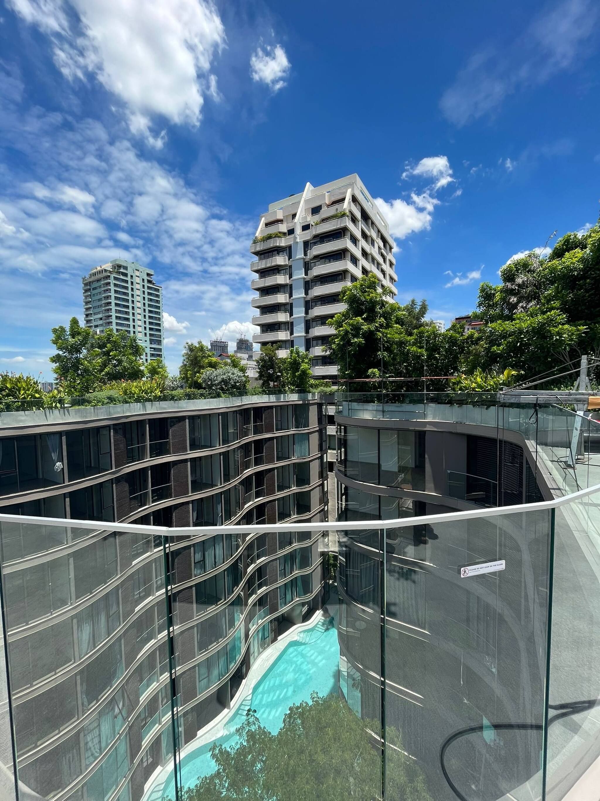 A modern building with a glass facade, a swimming pool, and a view of other high-rise buildings.