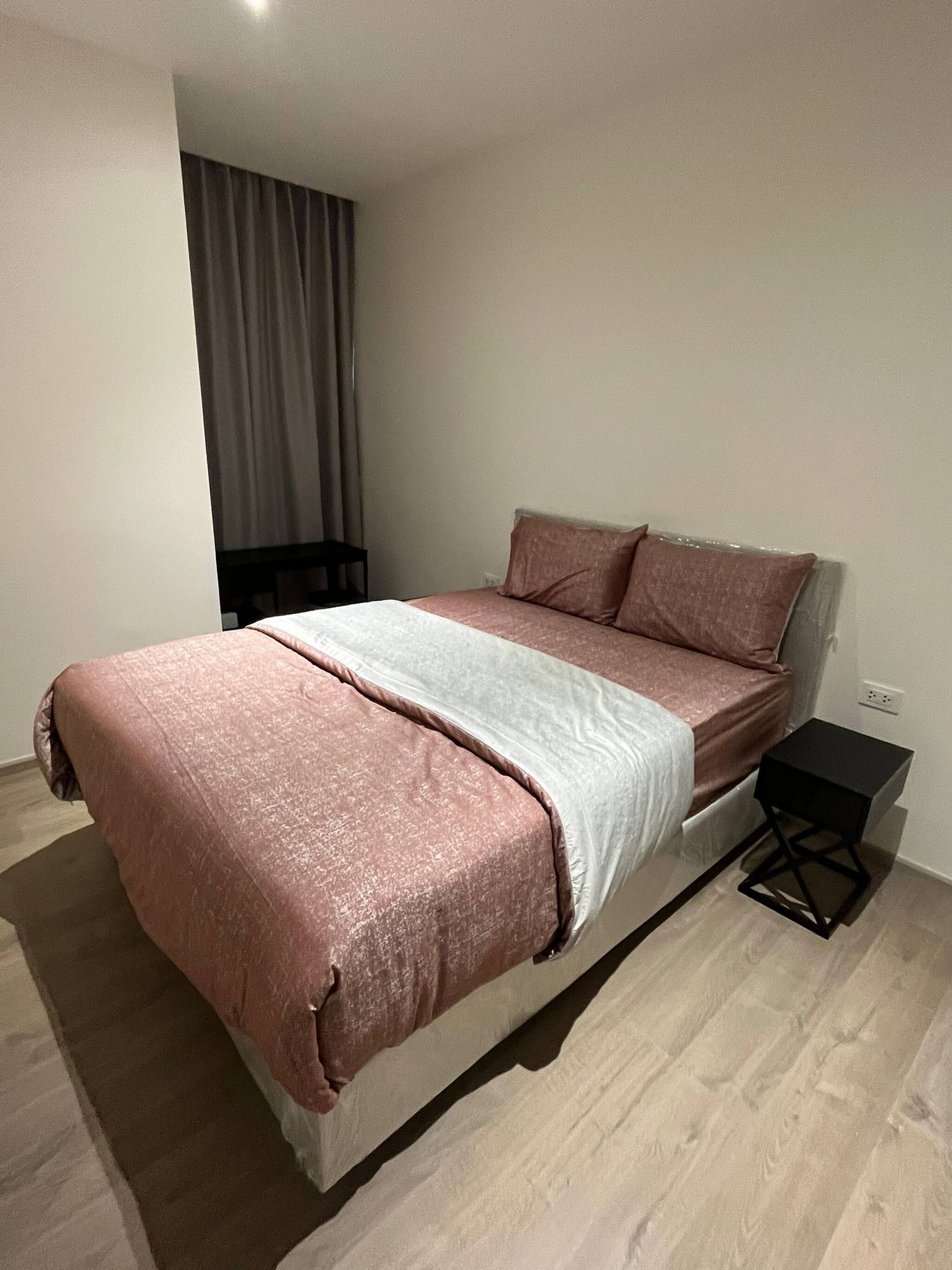 A modern bedroom with a bed, a small bedside table, and a window with curtains.