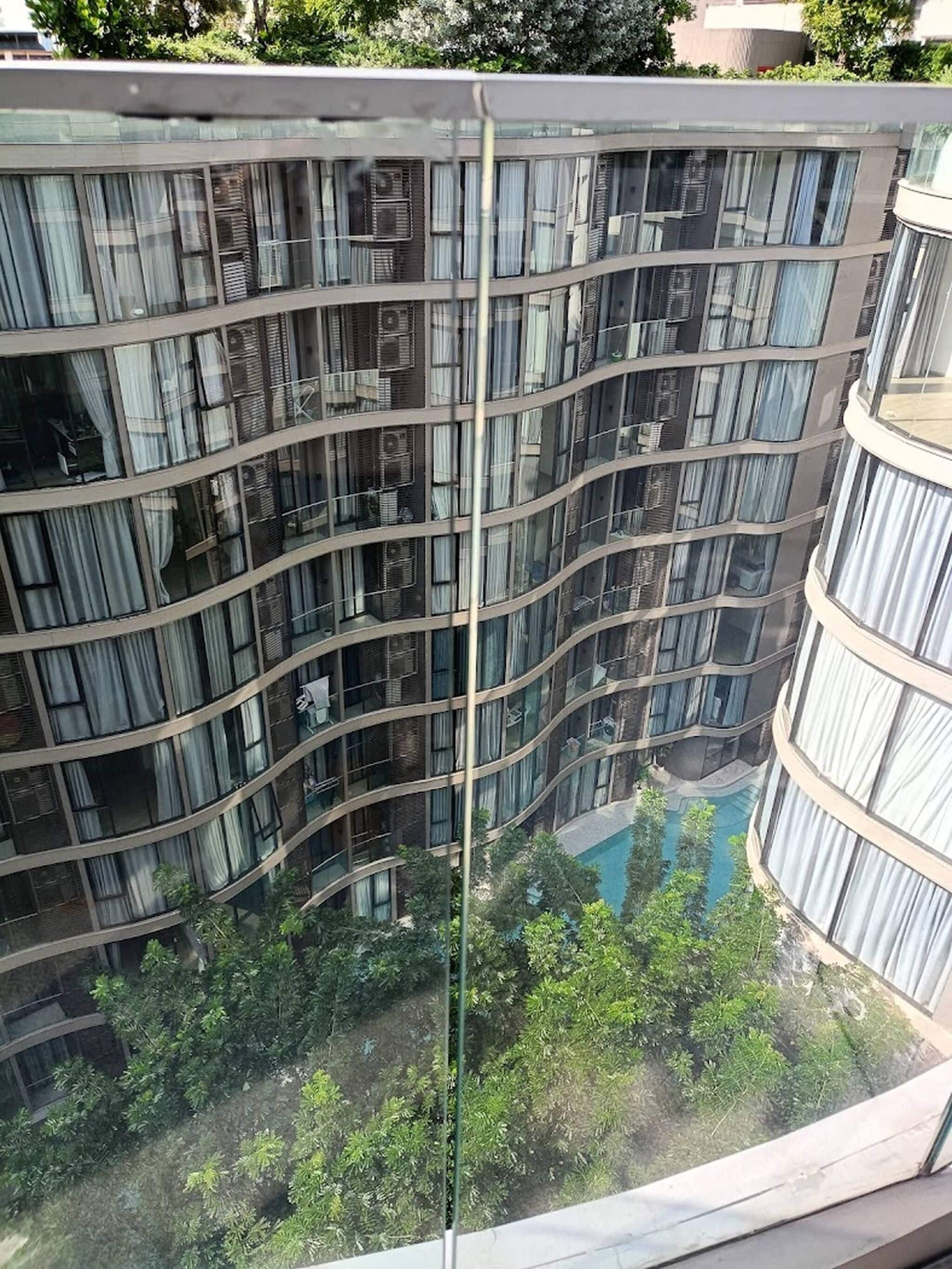 Un immeuble à plusieurs étages doté d’une façade incurvée, de grandes fenêtres et d’un espace piscine visible, agrémenté de verdure.
