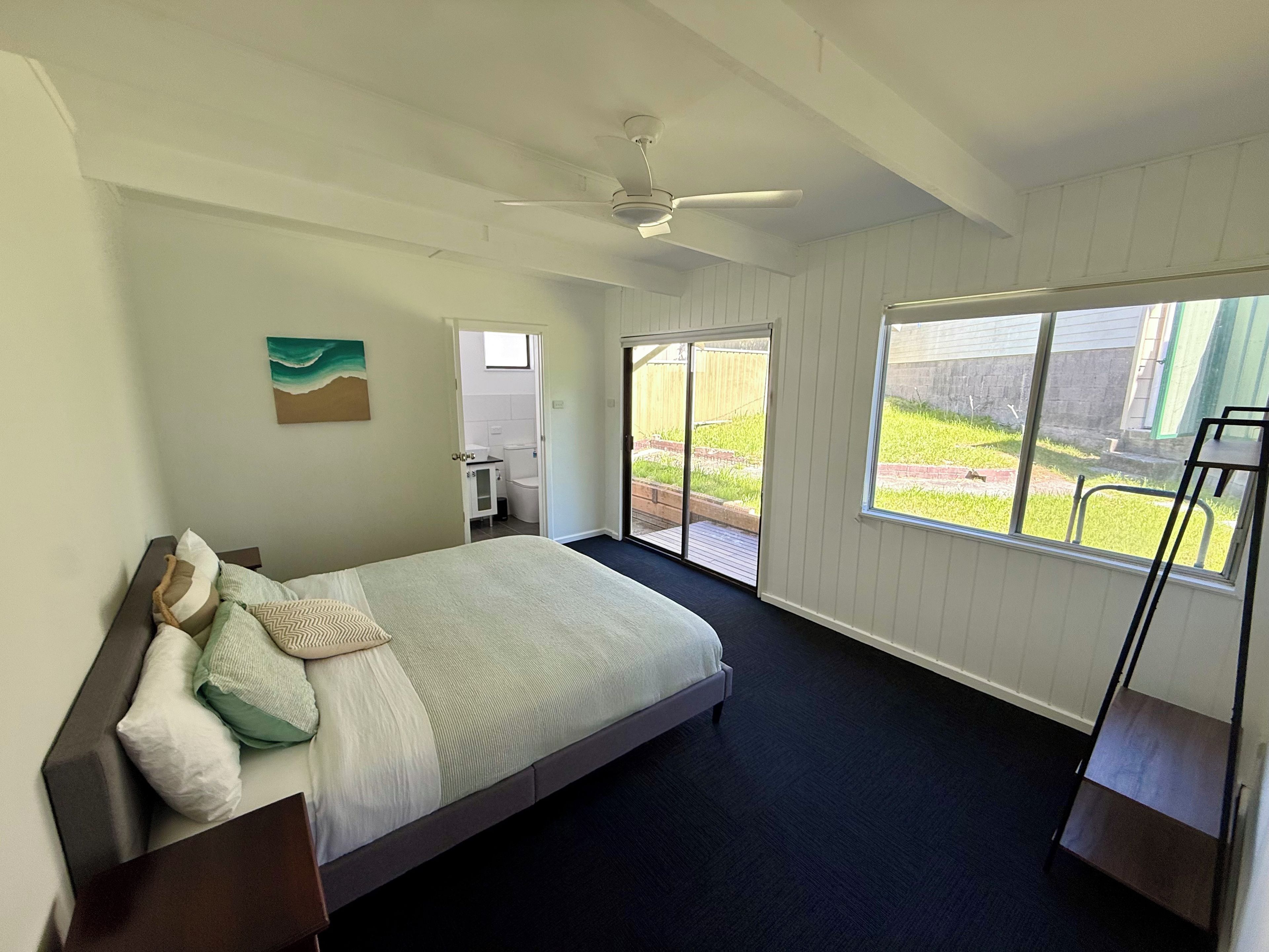 Een slaapkamer met een bed, een plafondventilator, een raam met uitzicht op het omliggende landschap en een deur naar de badkamer.