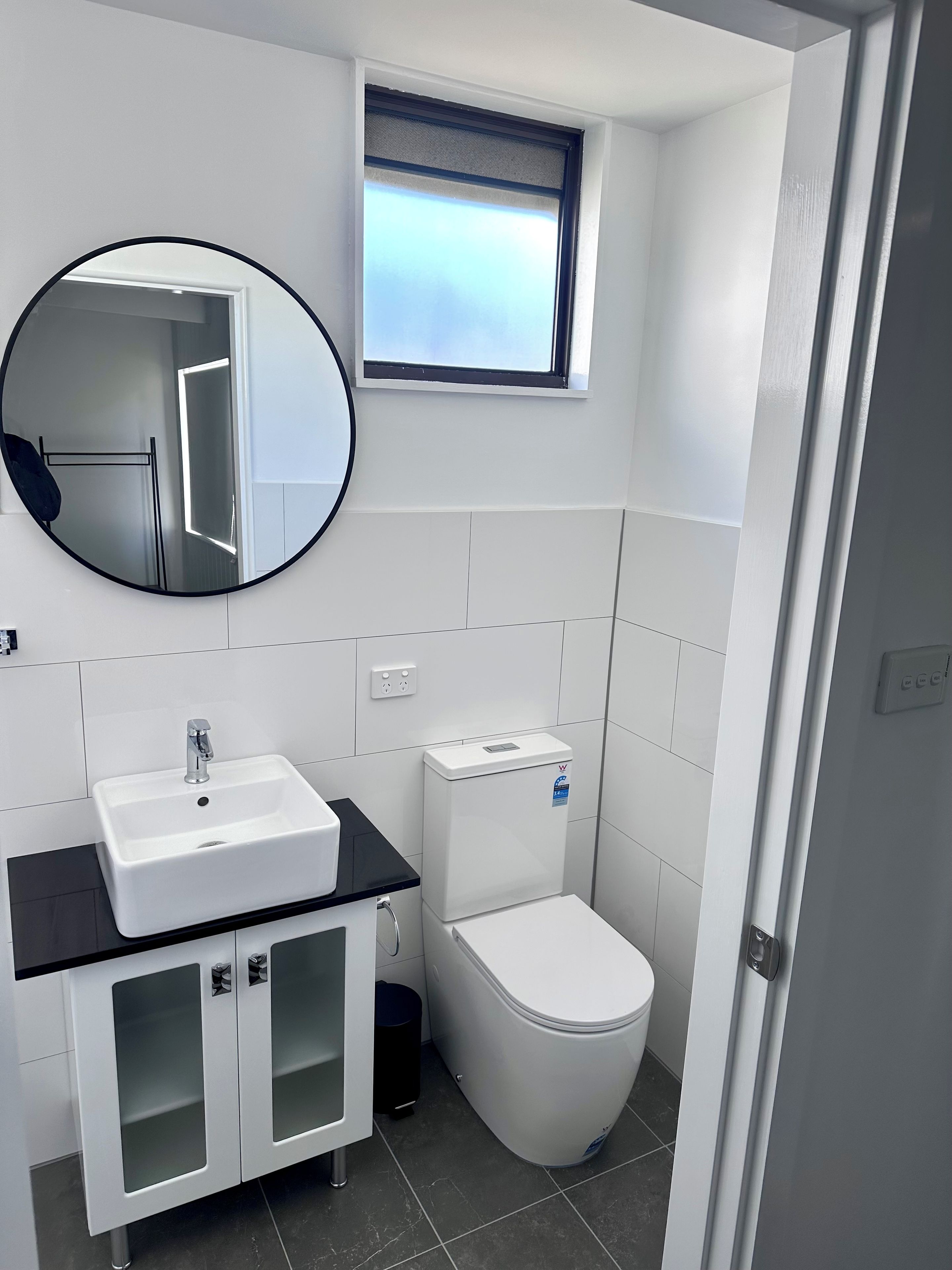 A modern bathroom with a white sink, toilet, and a round mirror.