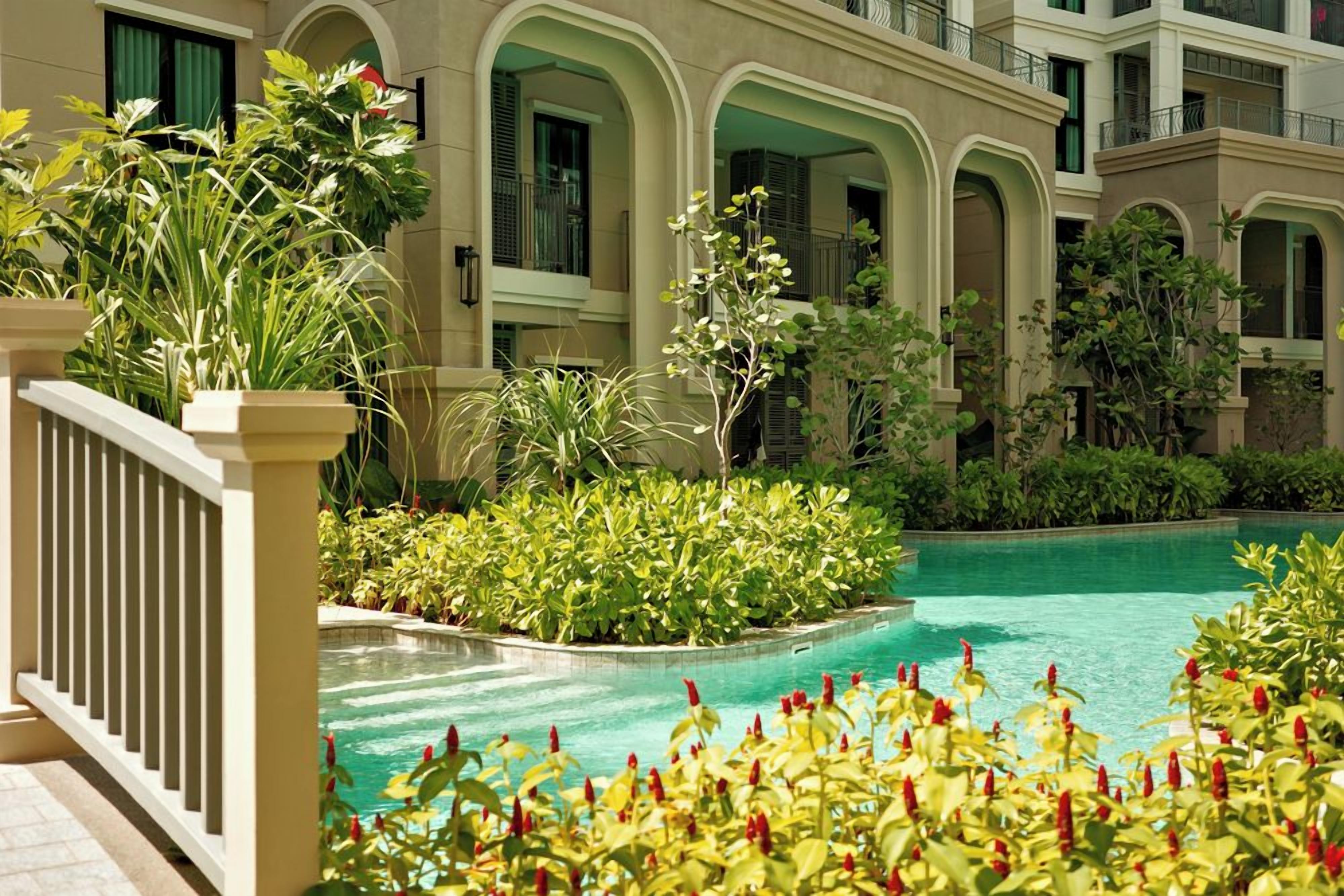 Un patio de hotel con piscina, rodeado de exuberante vegetación y un balustrada blanca.