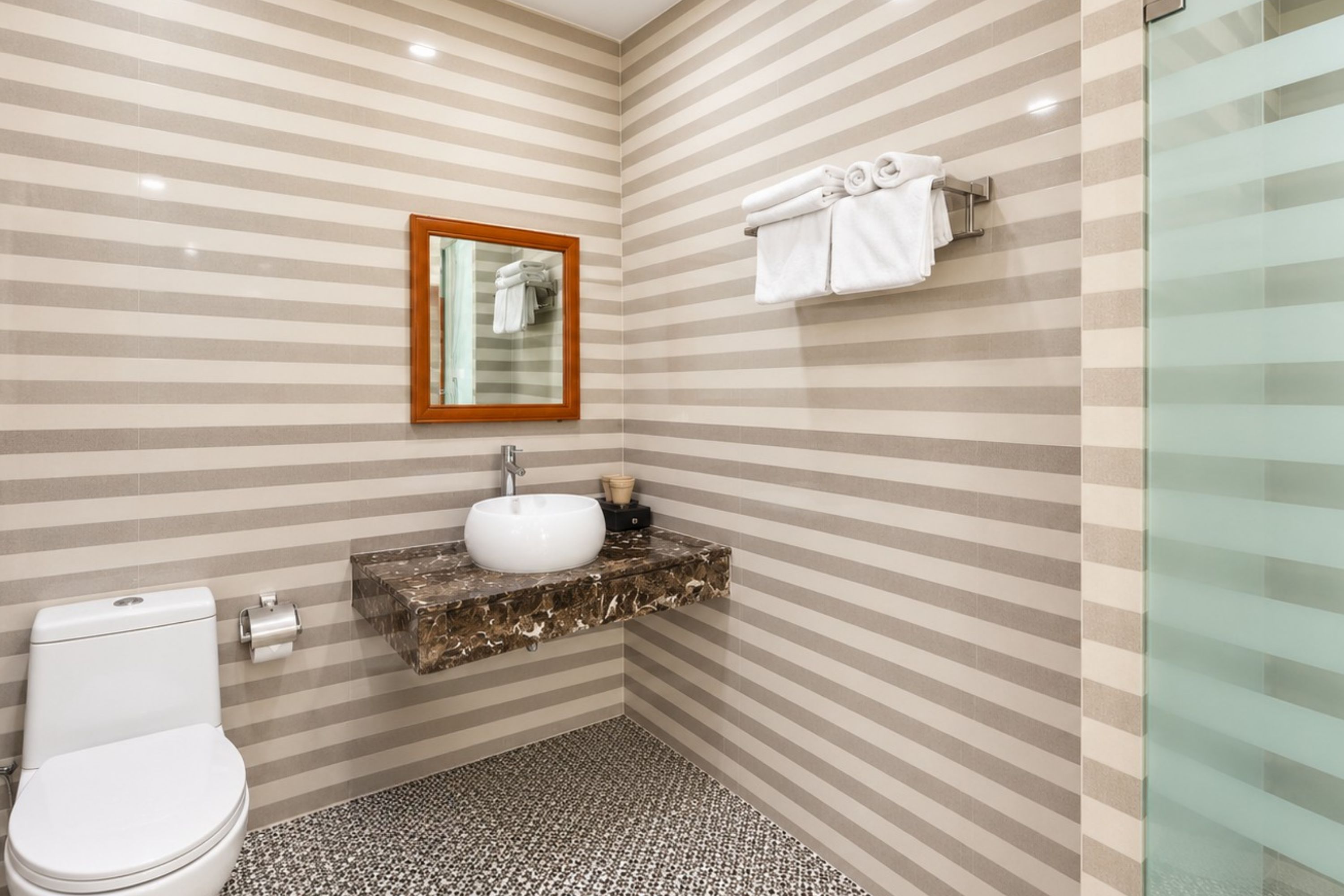 Casa de banho com parede com padrão riscado, lavatório branco, sanita e cabine de duche em vidro.