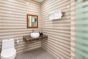 Casa de banho com parede com padrão riscado, lavatório branco, sanita e cabine de duche em vidro.