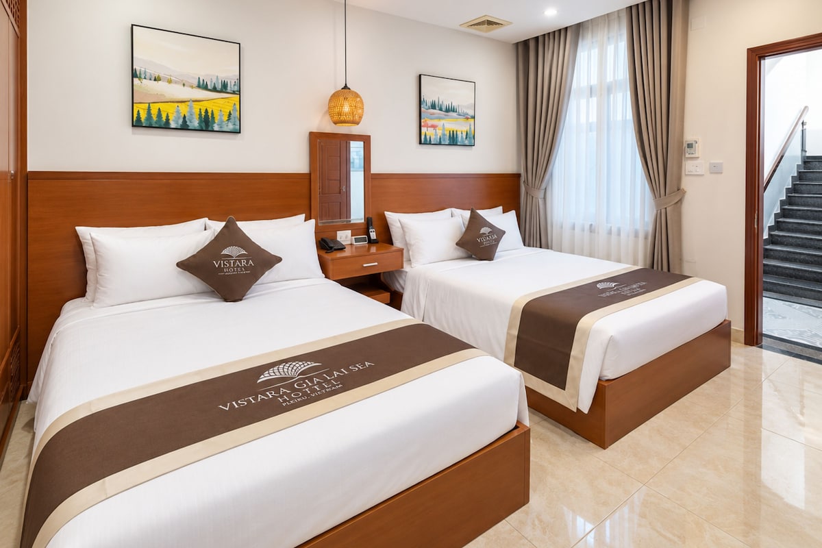 Quarto de hotel com duas camas, mesa de cabeceira, espelho e obras de arte nas paredes.
