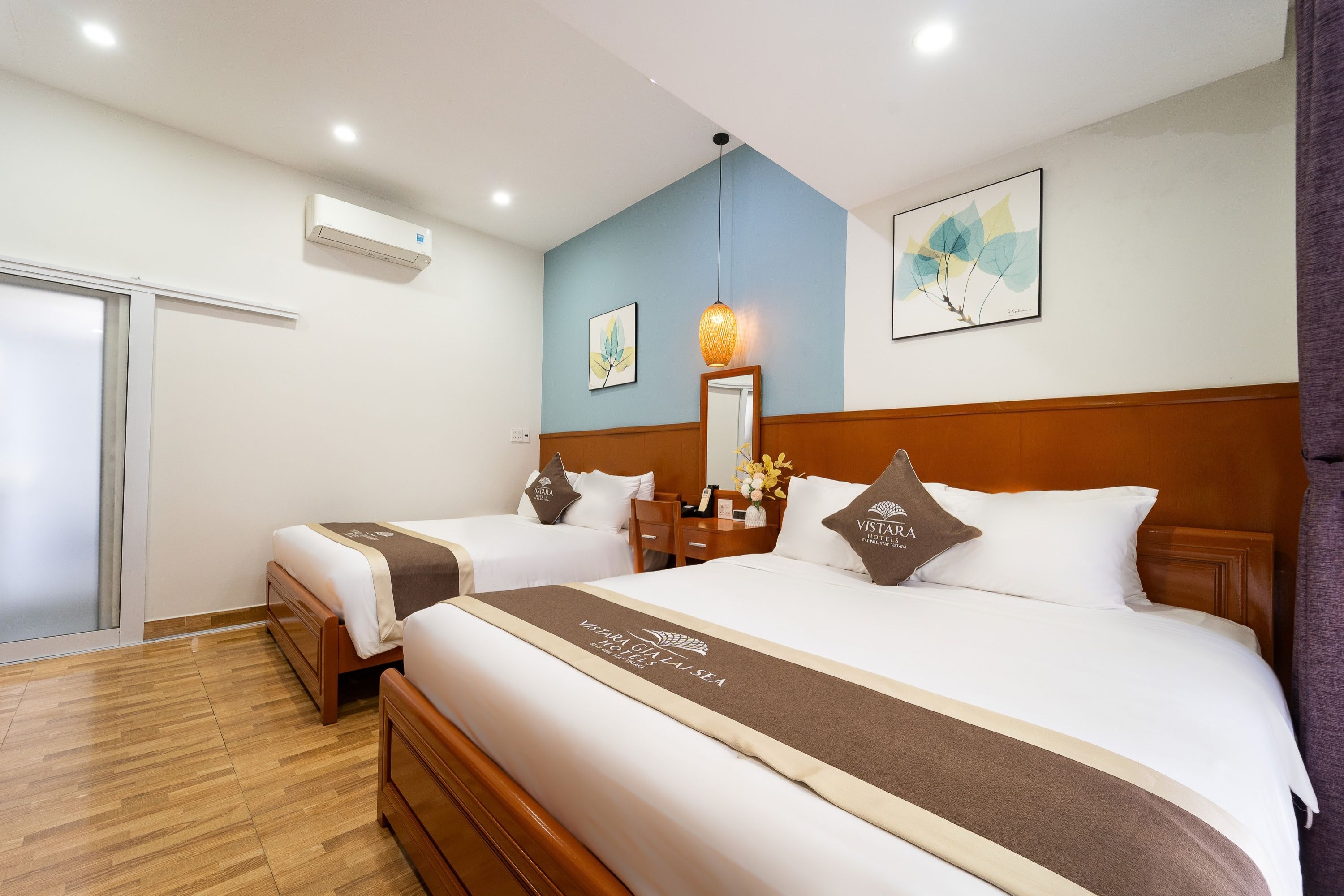 Quarto de hotel com duas camas, cabeceira de madeira, mesa de cabeceira, espelho e ar condicionado fixado na parede.