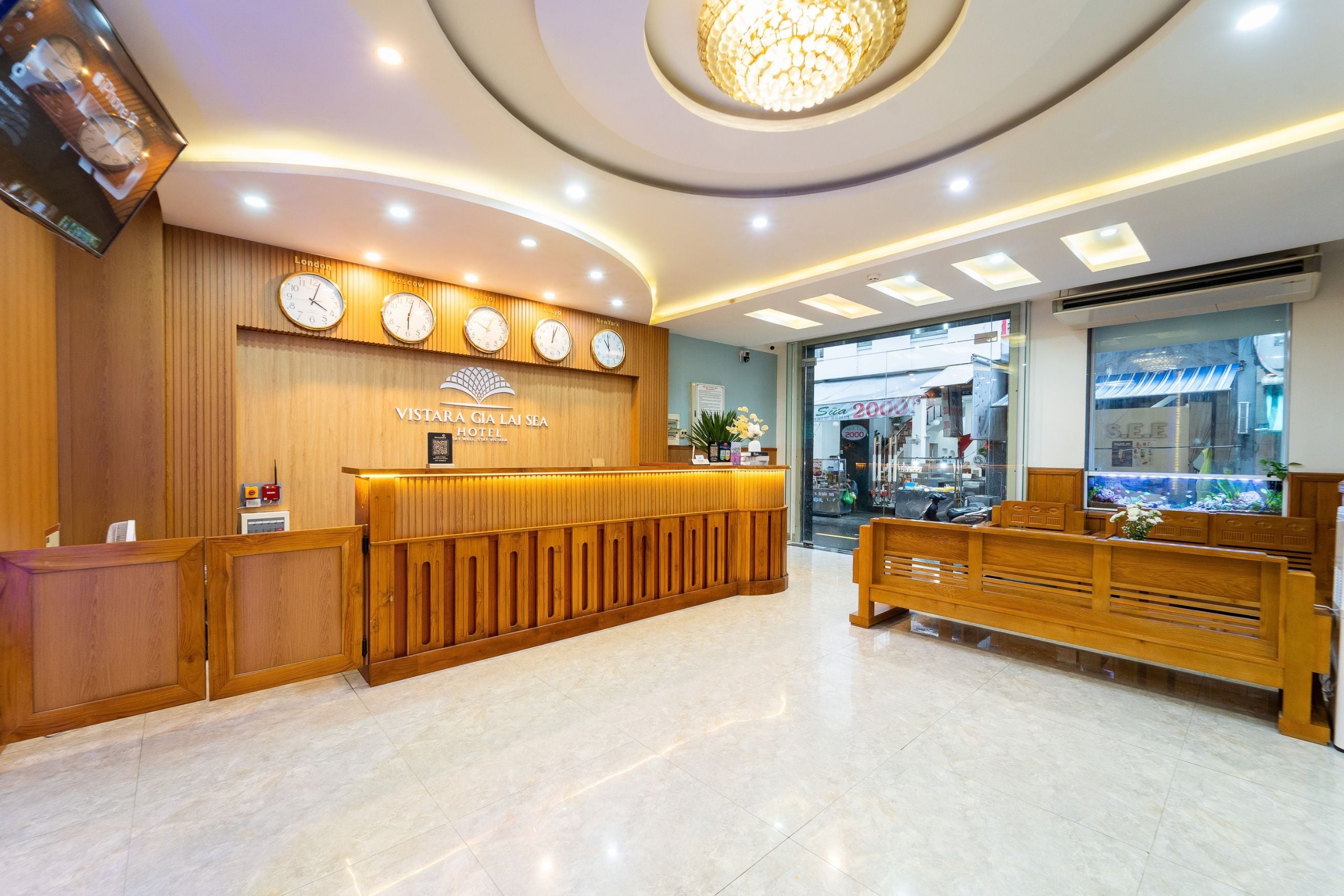 Zona de recepción de hotel con un mostrador de madera, varios relojes mostrando diferentes horarios de ciudades y un diseño de techo moderno.