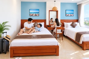 Quarto de hotel com cama, escrivaninha, cadeira, mala e planta.
