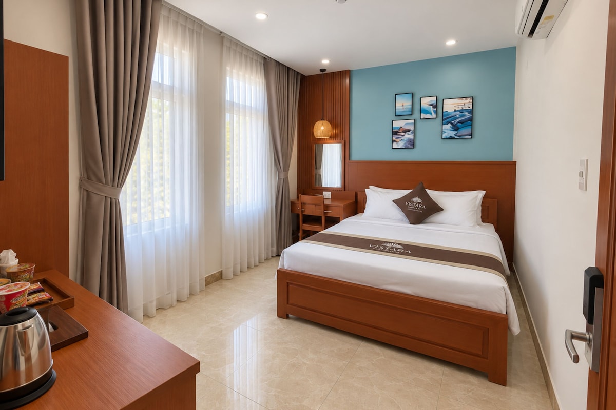 Quarto de hotel com cama, escrivaninha, cafeteira e vista para o exterior pela janela.