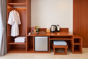 Quarto de hotel com escrivaninha de madeira, mini-frigorífico, chaleira e um pequeno espaço para sentar.