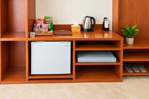 Una kitchenette compacta con un refrigerador miniatura, hervidor de agua, cafetera y una pequeña planta.