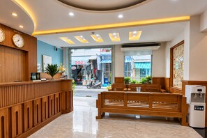 Zona de recepción de un hotel con un mostrador de madera, un reloj y un área de estar con bancos.