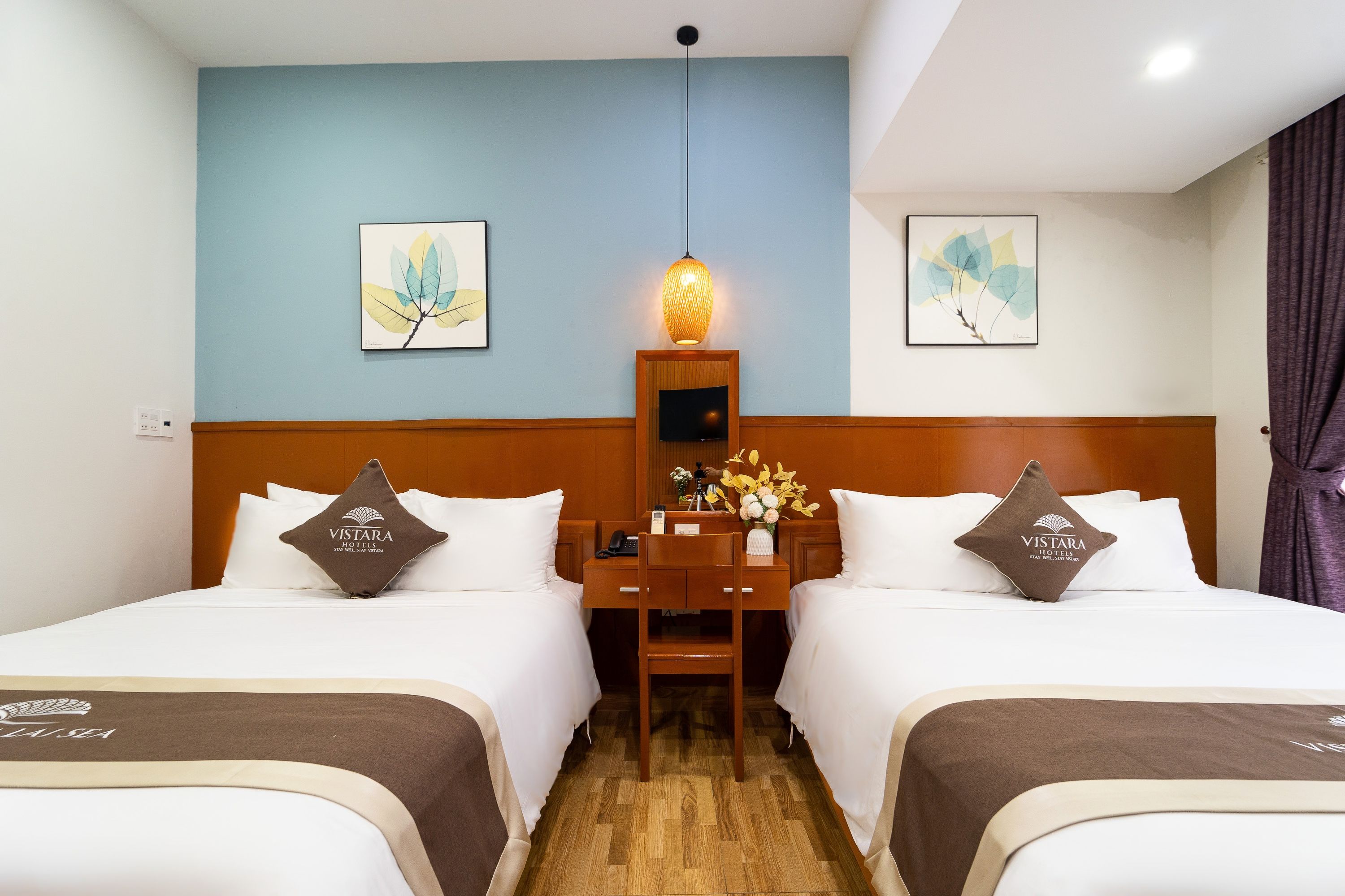 A hotel room with two beds, a desk, a telephone, and a lamp.
