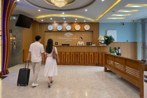 Una recepción de hotel con un reloj, una pantalla digital y una recepcionista.