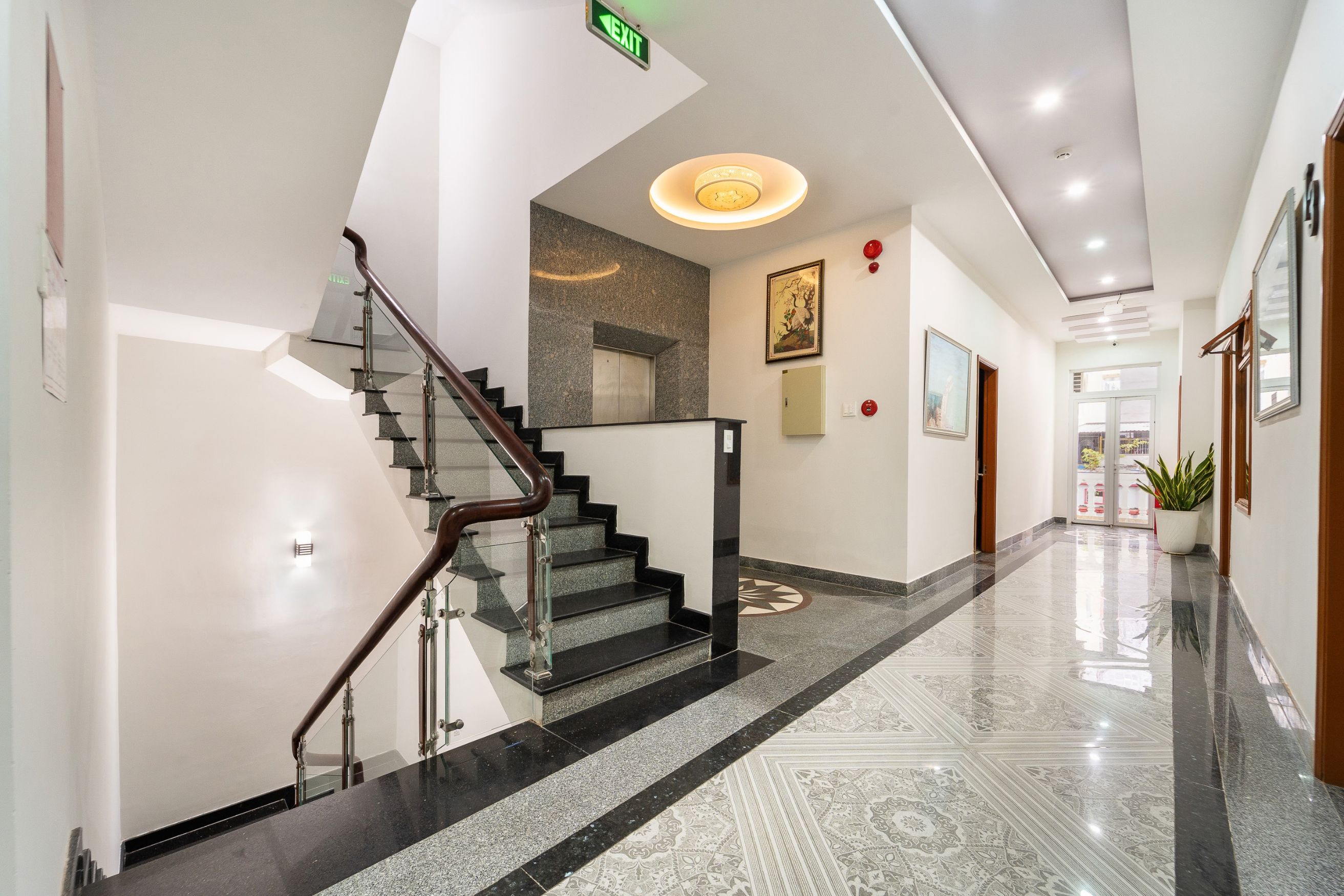 Um hall de hotel moderno com escadaria de vidro, balcão de recepção e piso estampado.
