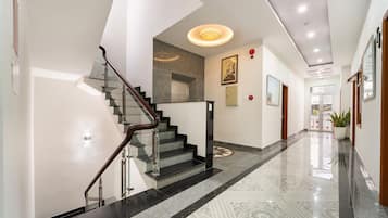 Um hall de hotel moderno com escadaria de vidro, balcão de recepção e piso estampado.