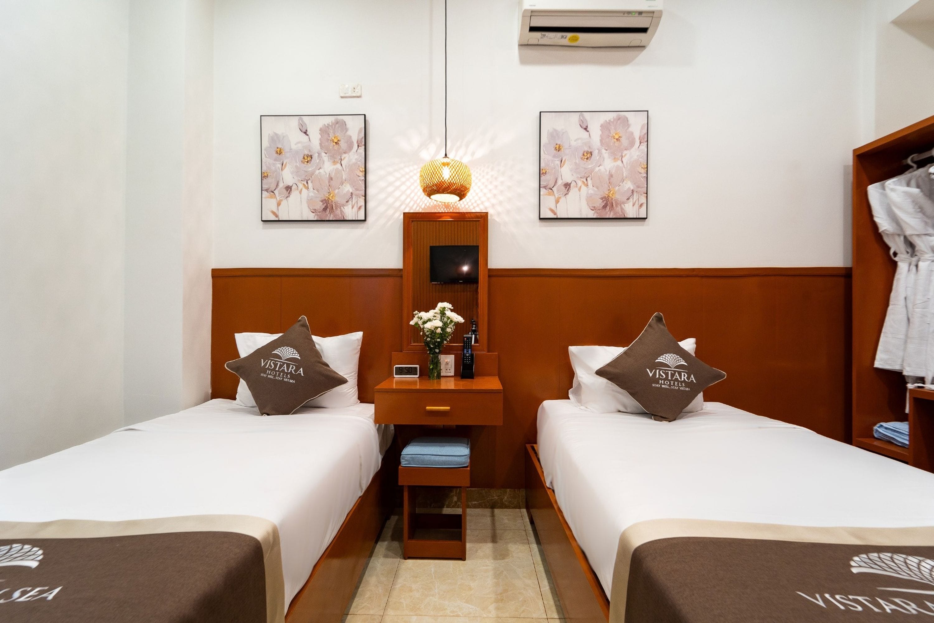 A hotel room with two beds, a nightstand, a TV, and a wall-mounted air conditioner.