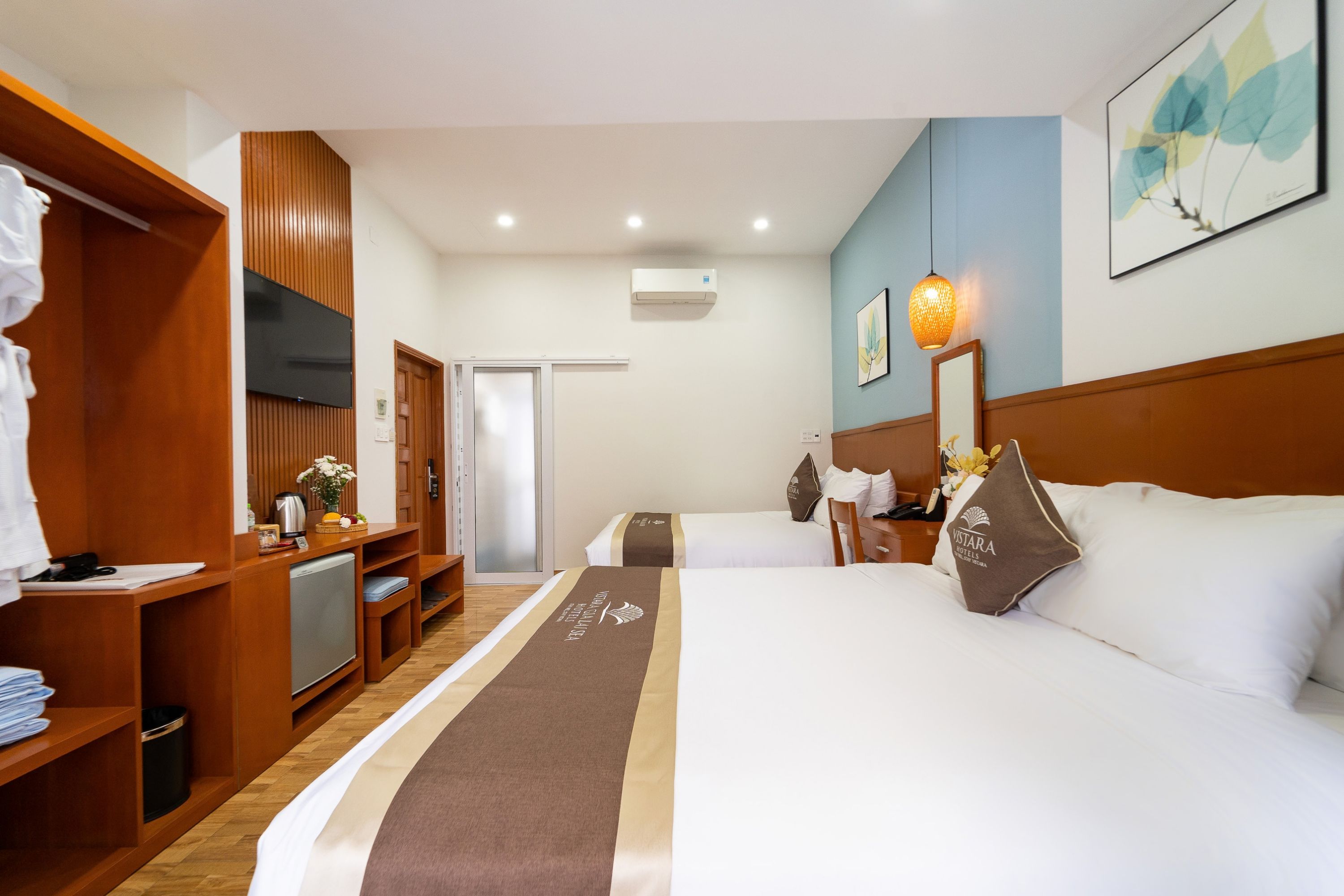 A hotel room with two beds, a desk, a wardrobe, and a television.