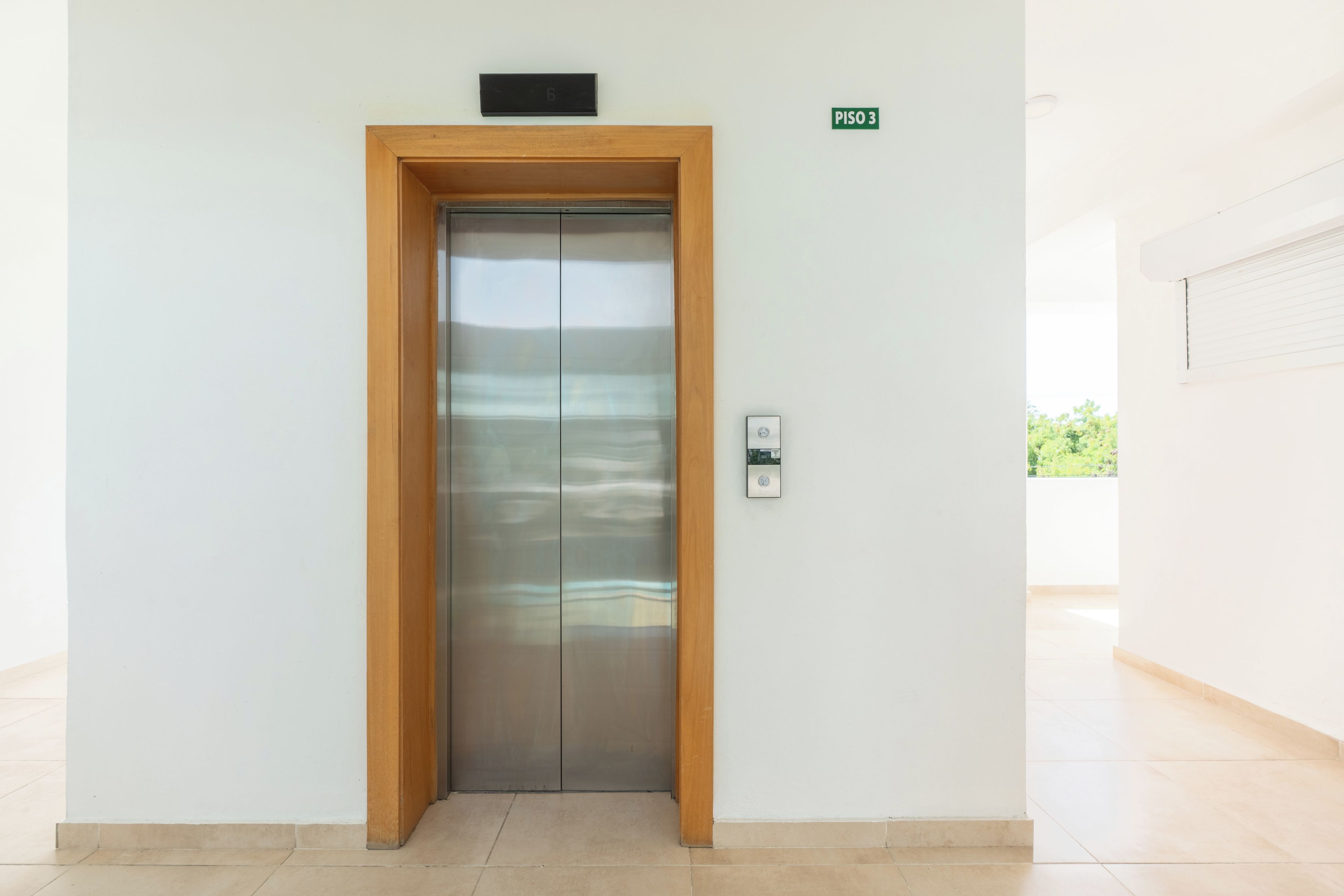 Um elevador moderno com estrutura de madeira, visor digital e campainha.