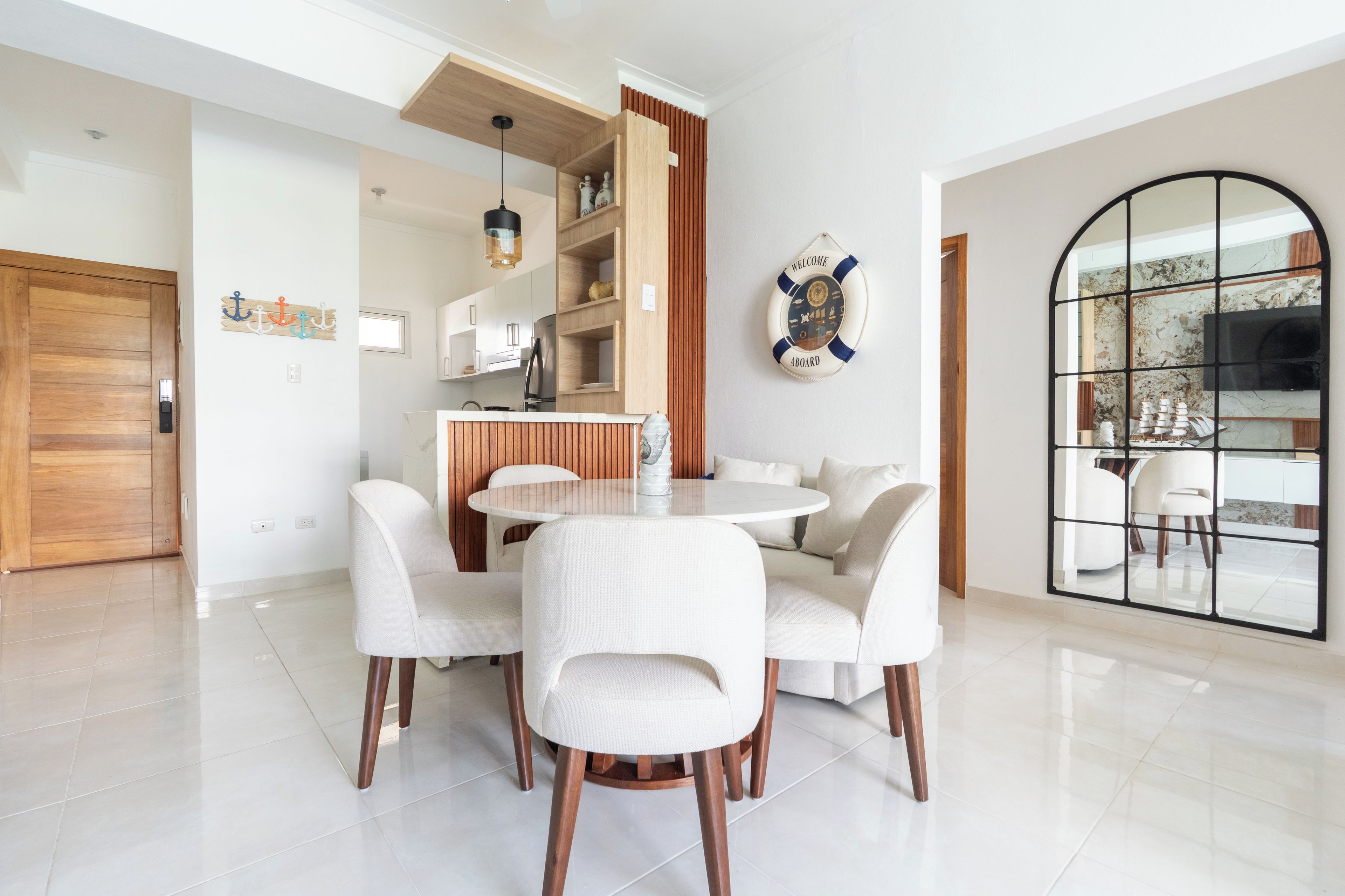 Un comedor moderno con una mesa redonda y cuatro sillas, una cocina con armarios de madera y un gran ventanal arqueado.