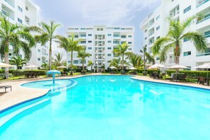 Una piscina rodeada de palmeras y sillas de descanso, con un edificio moderno al fondo.