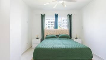 Quarto com cama, ventilador de teto e janela com cortinas.