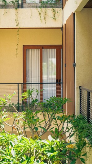 A building with a balcony, a door with a window, and some greenery in the foreground. - Tedu Hotel (Canggu)