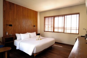 A bedroom with a wooden headboard, a large bed with white bedding, a bedside table, and a window with blinds. - Tedu Hotel (Canggu)