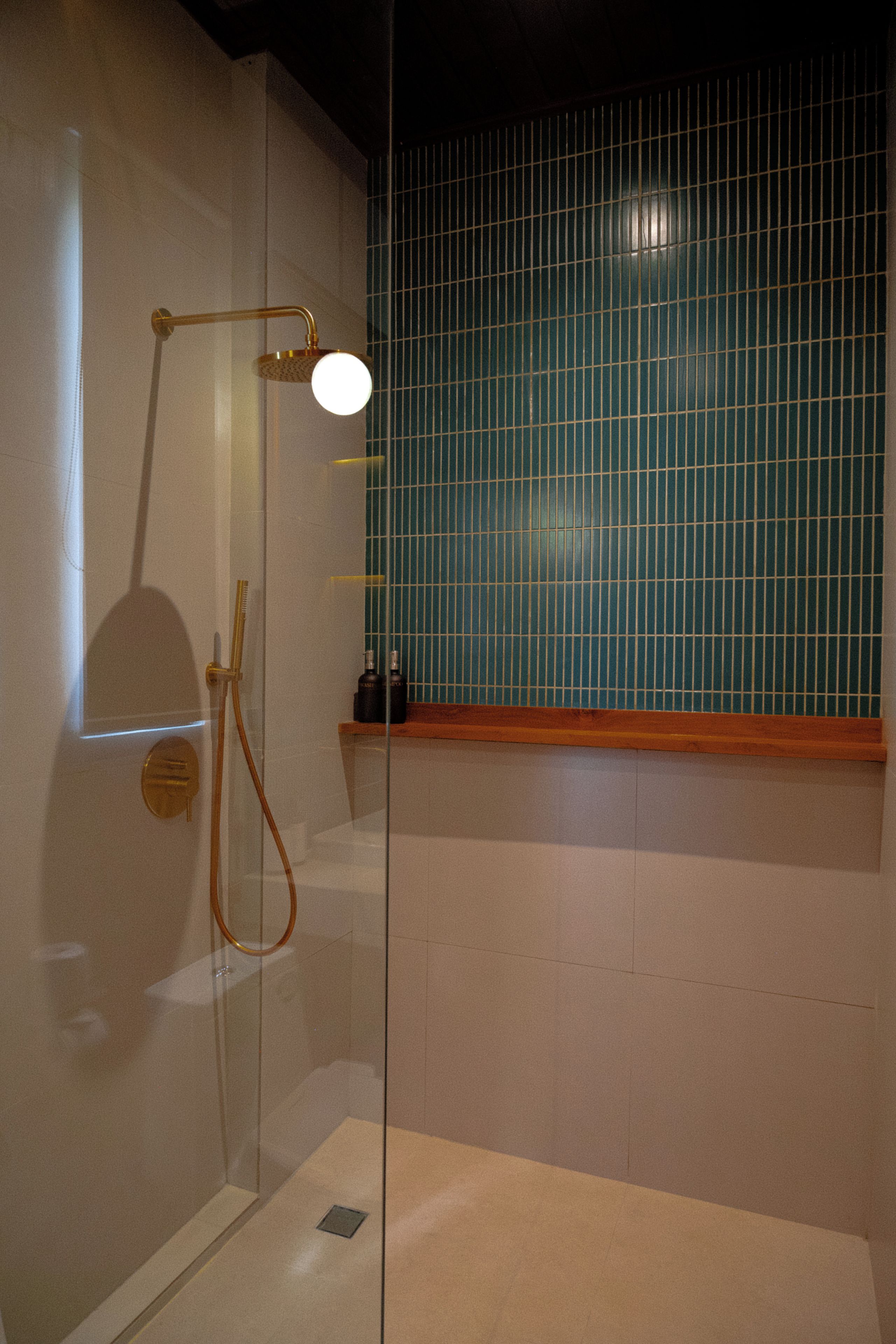 A glass-enclosed shower with a gold showerhead and a wall-mounted faucet.