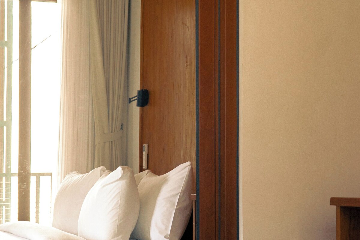 A hotel room with a bed, a wooden panel wall, and a window with curtains.